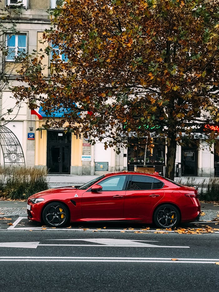 A sleek red sports car parked on a city street lined with autumn trees.
